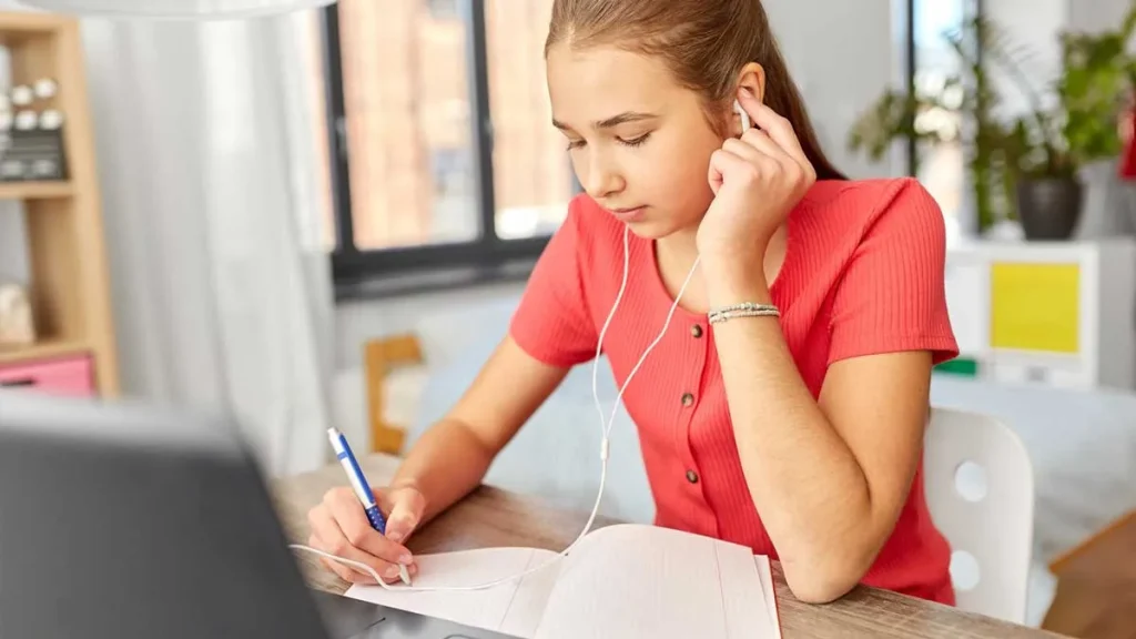 دختری در حال گوش دادن به صوت و یادداشت برداری همزمان به عنوان یکی ازمراحل تقویت مهارت شنیداری